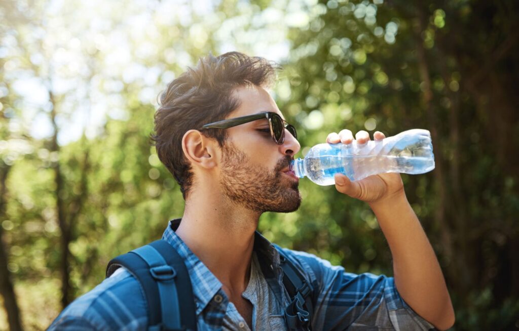 A man drinking from a bottle of water in the forest.